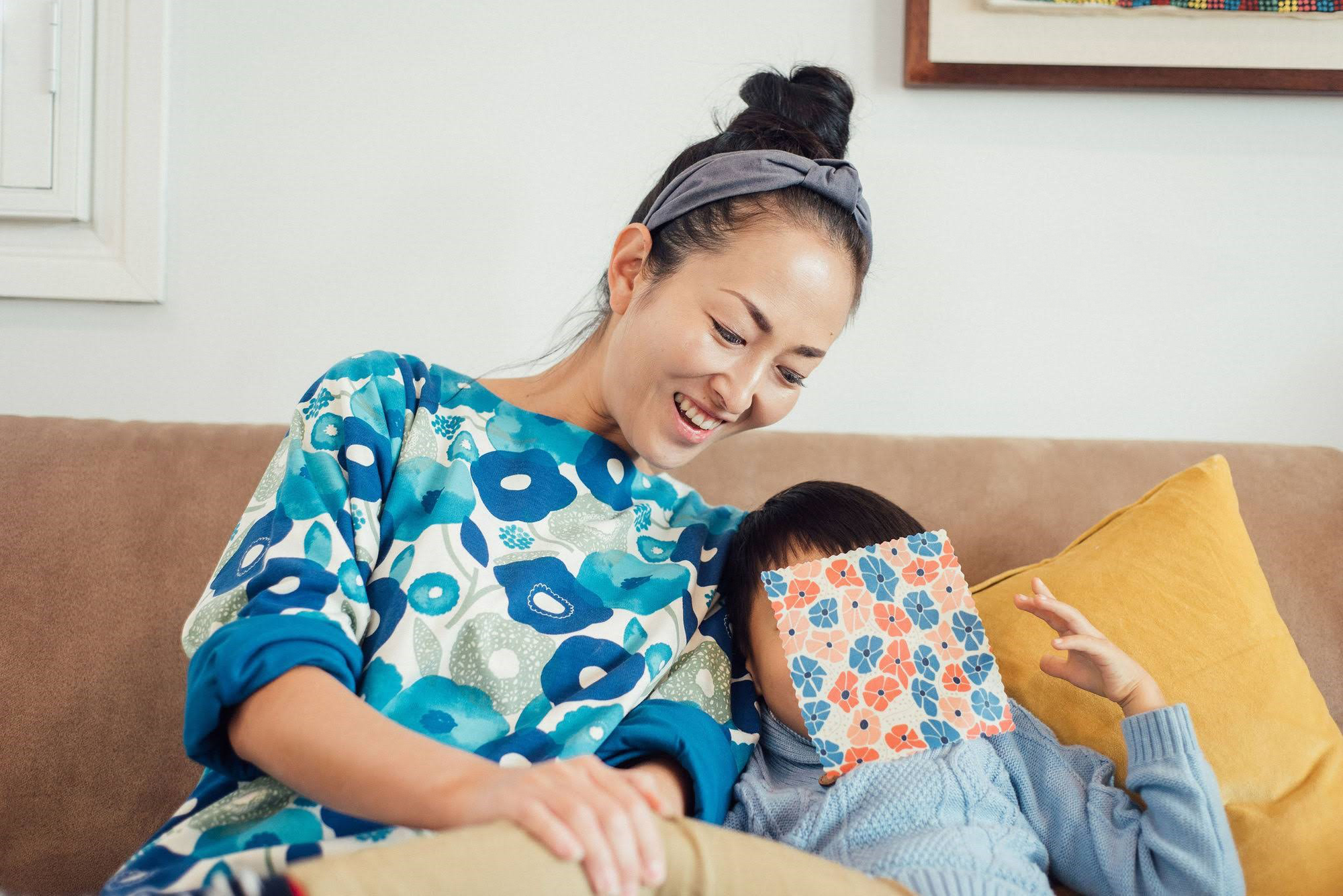 笑顔で大人の女性と小さな男の子が並んでソファに座っていて、男の子は顔にみつろうラップを載せている